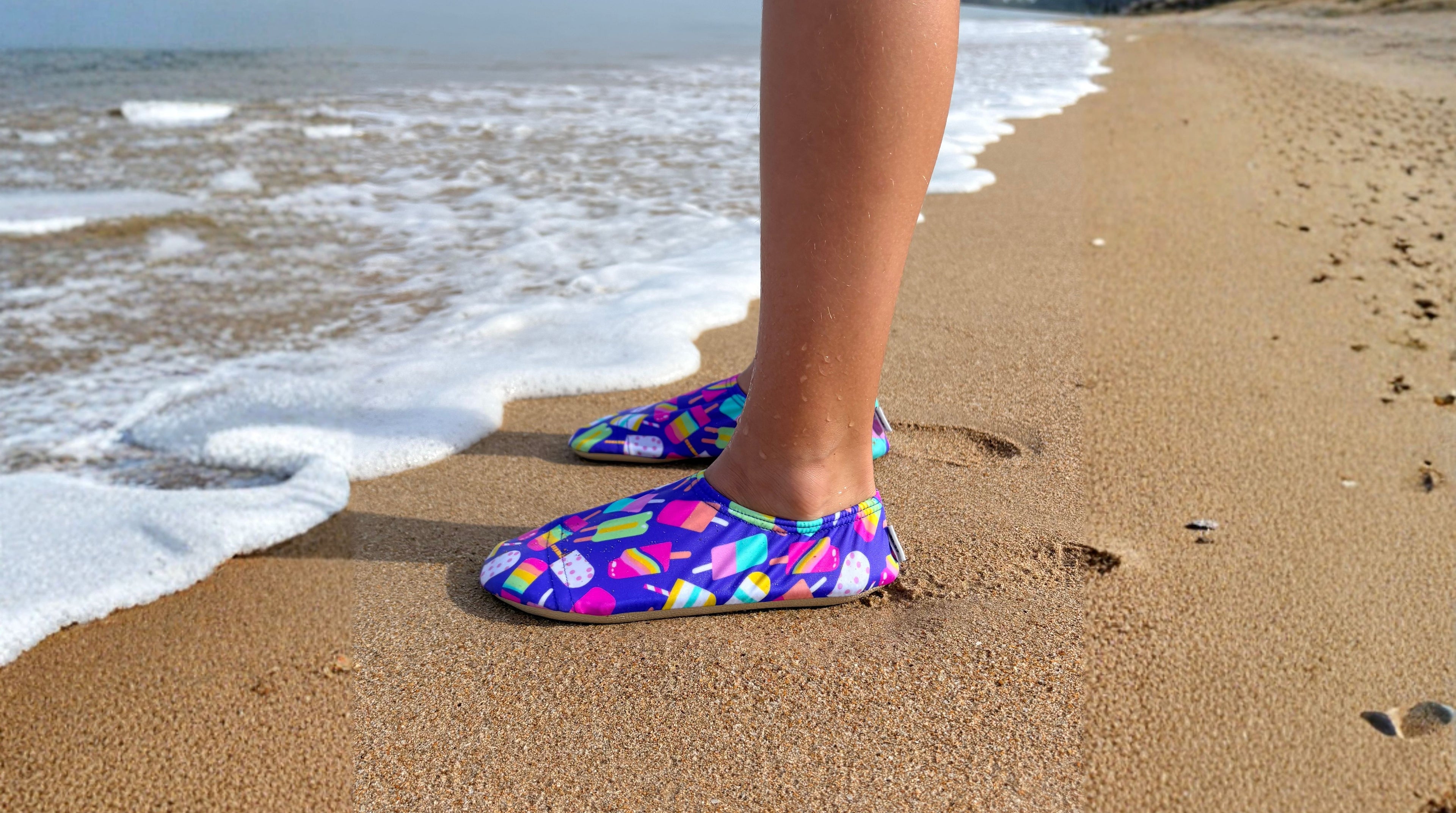 Toddler standing on a sandy beach with non-slip water socks on.