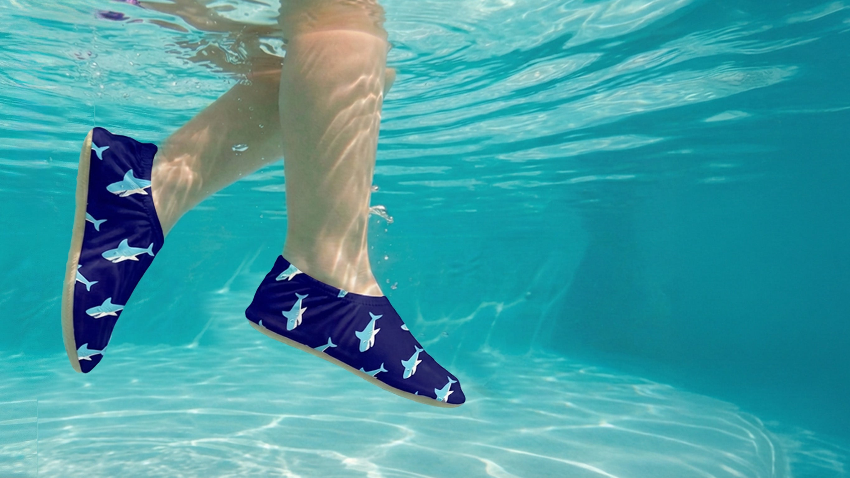 Toddler wearing blue shark-patterned water shoes in clear pool water