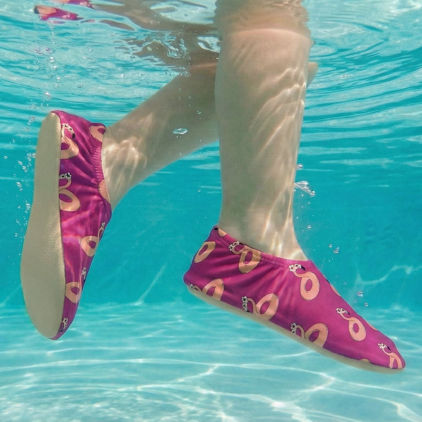 Pink non-slip water socks with flamingo designs worn underwater.