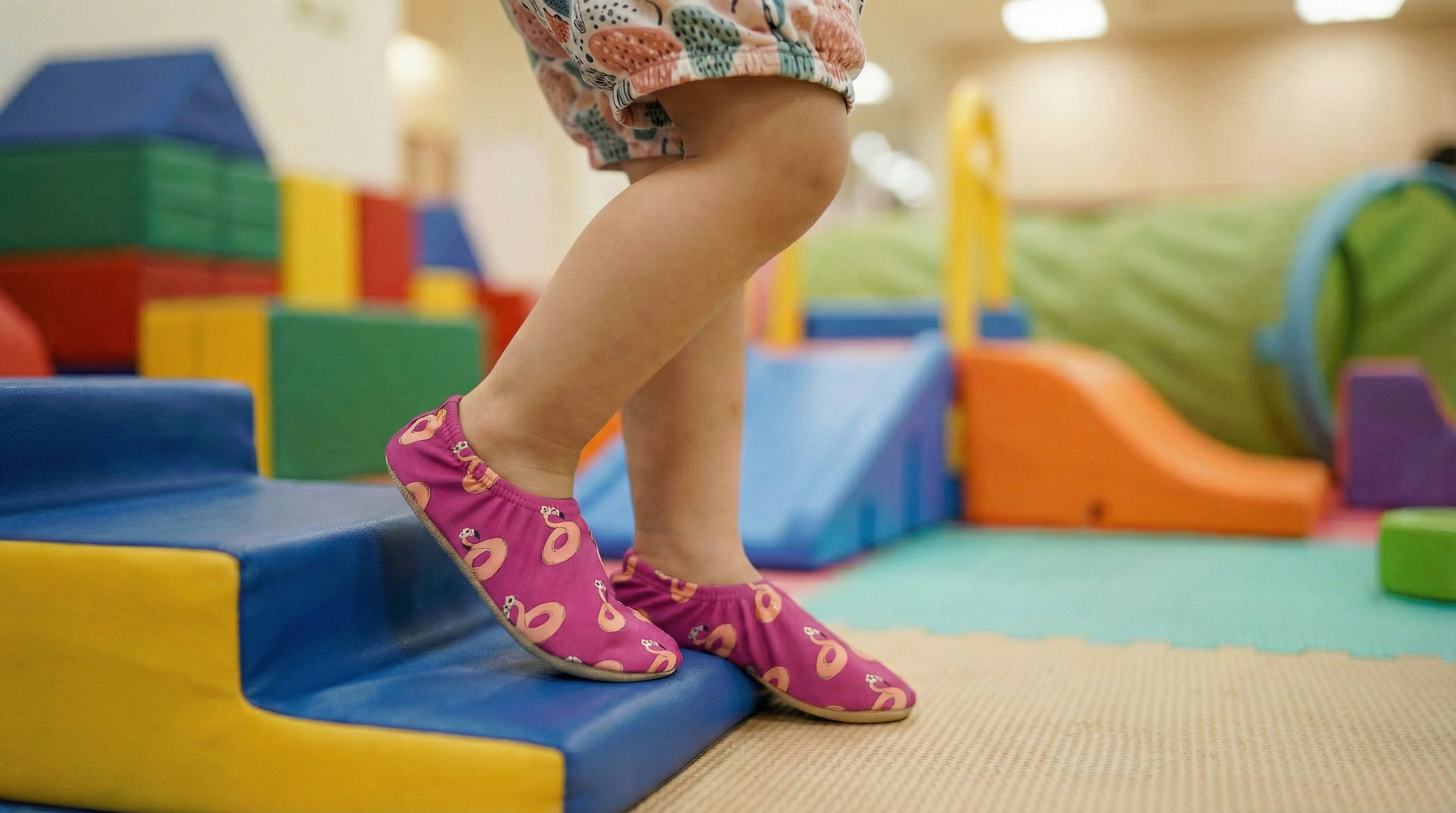 Child wearing pink non-slip socks with flamingo patterns on a colorful playground.