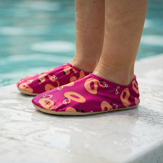 Child wearing pink non-slip water socks with peach flamingo patterns by a Singapore pool.
