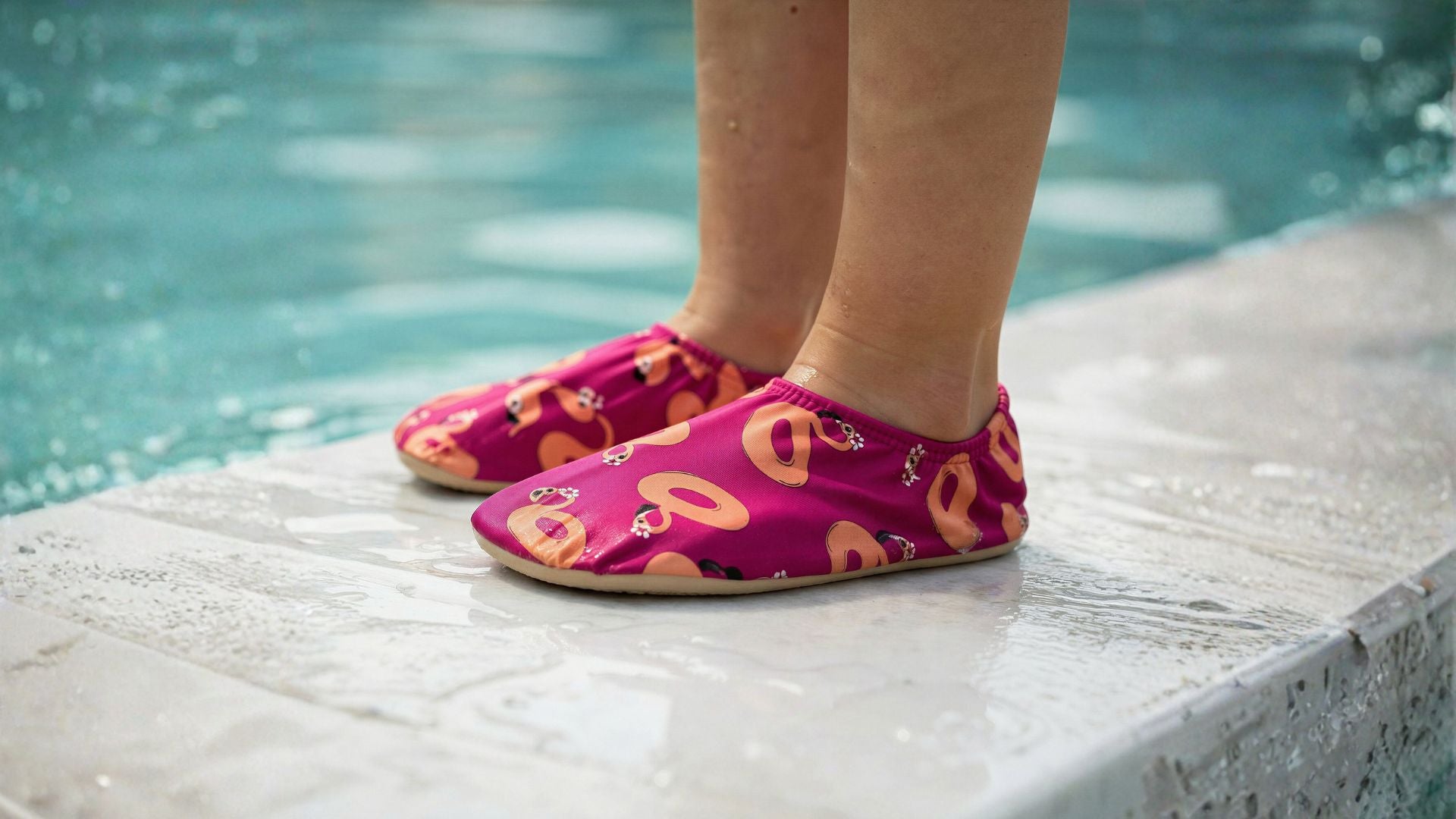Child wearing pink non-slip water socks with peach flamingo patterns by a Singapore pool.