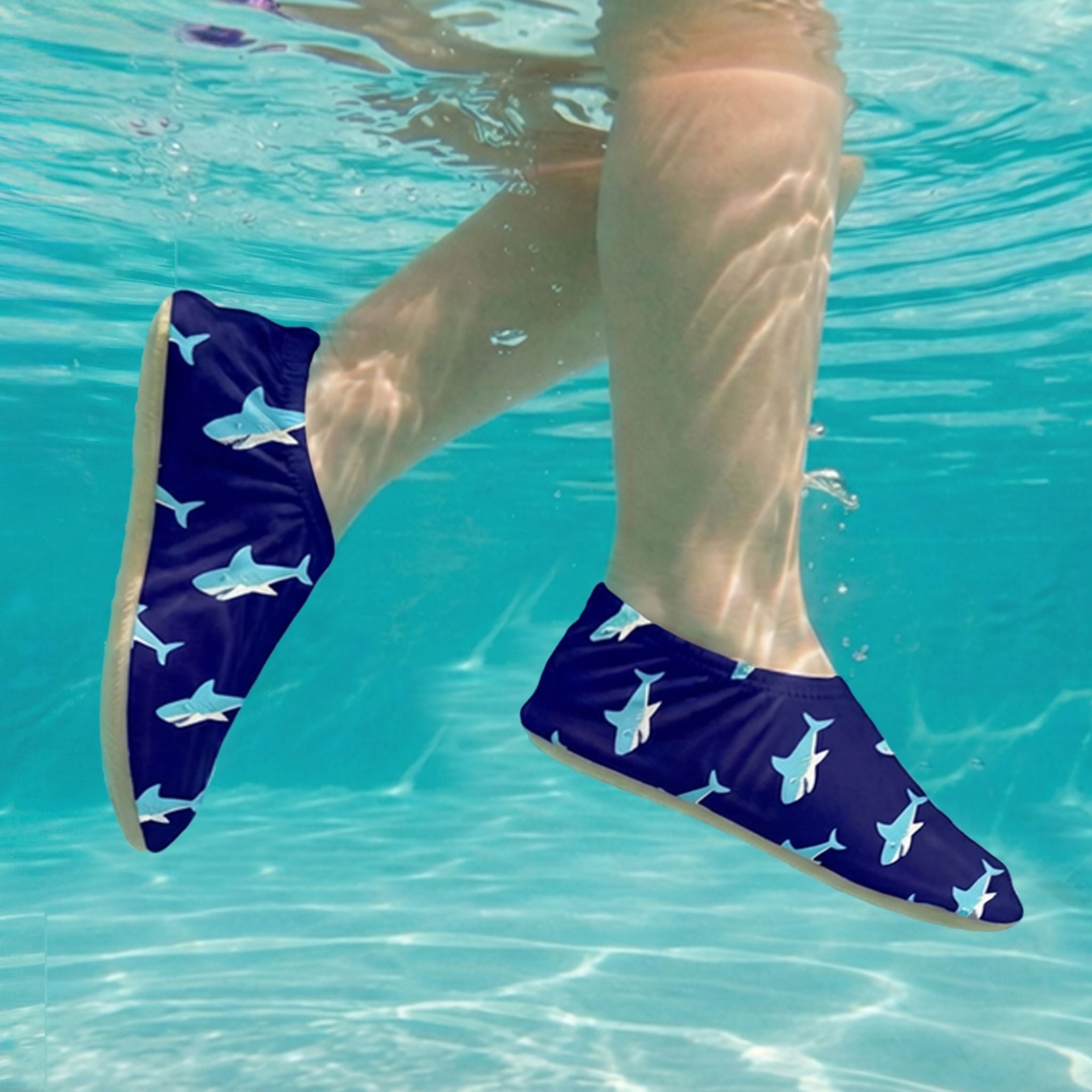 Child wearing shark-patterned blue non-slip water sock in clear blue water.